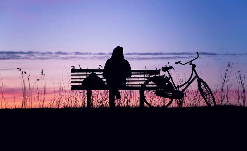 Henkilö istuu yksin penkillä hämärässä auringonlaskun aikaan.